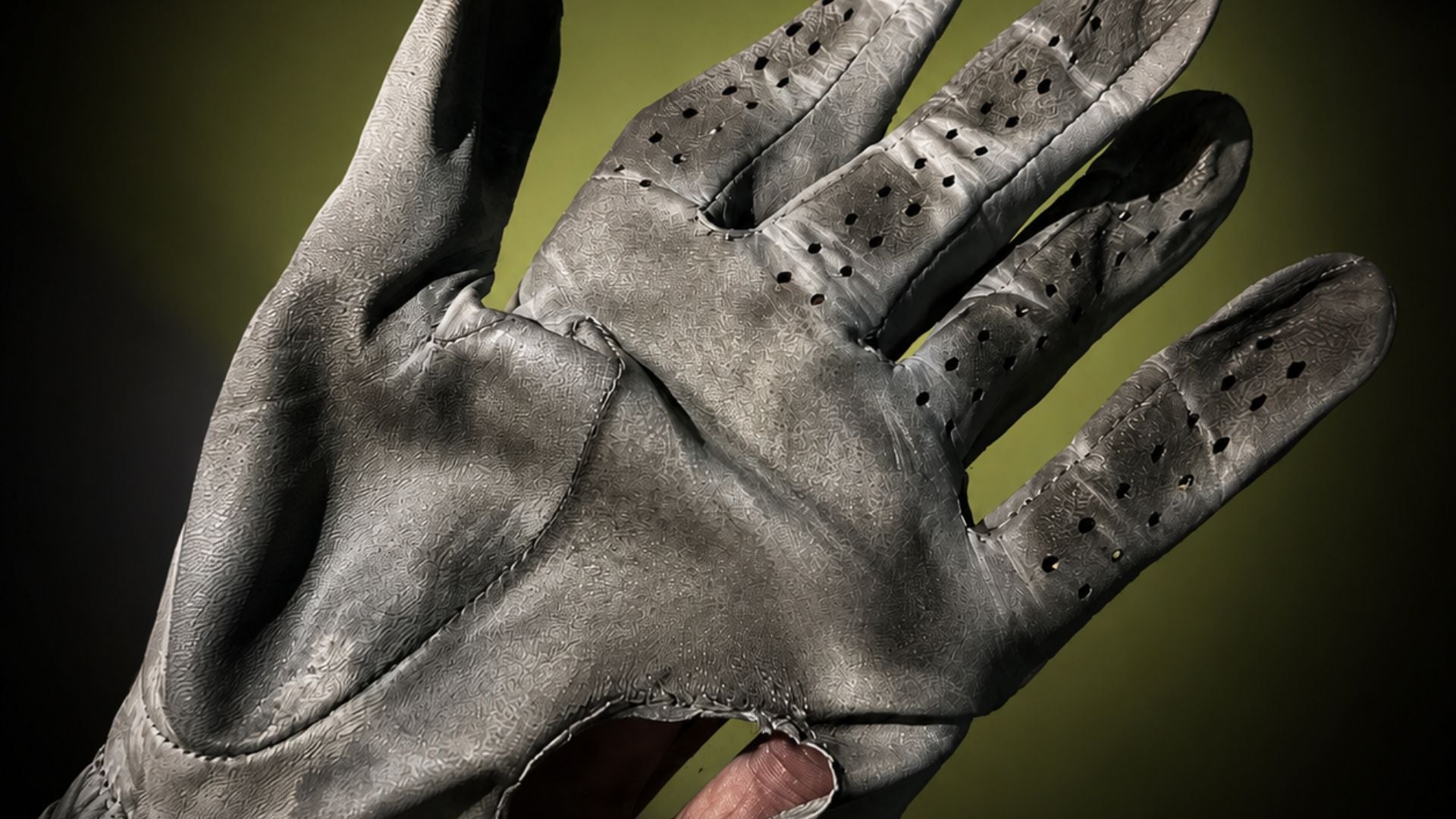 Worn leather golf glove with whole in the palm